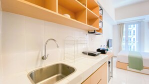 A modern kitchen with a stainless steel sink, white tiled backsplash, and wooden shelves above. - Good Cozy Living Studio Apartment At Tokyo Riverside Pik 2 (Teluknaga)
