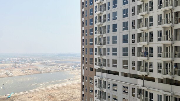 A high-rise building with multiple balconies and a view of a construction site and water body in the background. - Good Cozy Living Studio Apartment At Tokyo Riverside Pik 2 (Teluknaga)