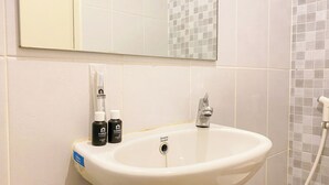 A bathroom with a white sink, a mirror above it, and a shower area with tiled walls. - Good Cozy Living Studio Apartment At Tokyo Riverside Pik 2 (Teluknaga)