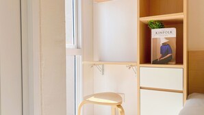 A minimalist room with a wooden desk, a stool, and a bookshelf containing a book titled 'KINFOLK'. - Good Cozy Living Studio Apartment At Tokyo Riverside Pik 2 (Teluknaga)