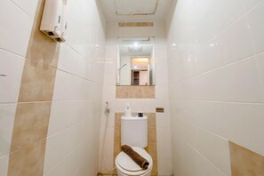 Ein kleines Badezimmer mit Fliesen, einer Toilette, einem Handtrockner und einem Spiegel über der Toilette.