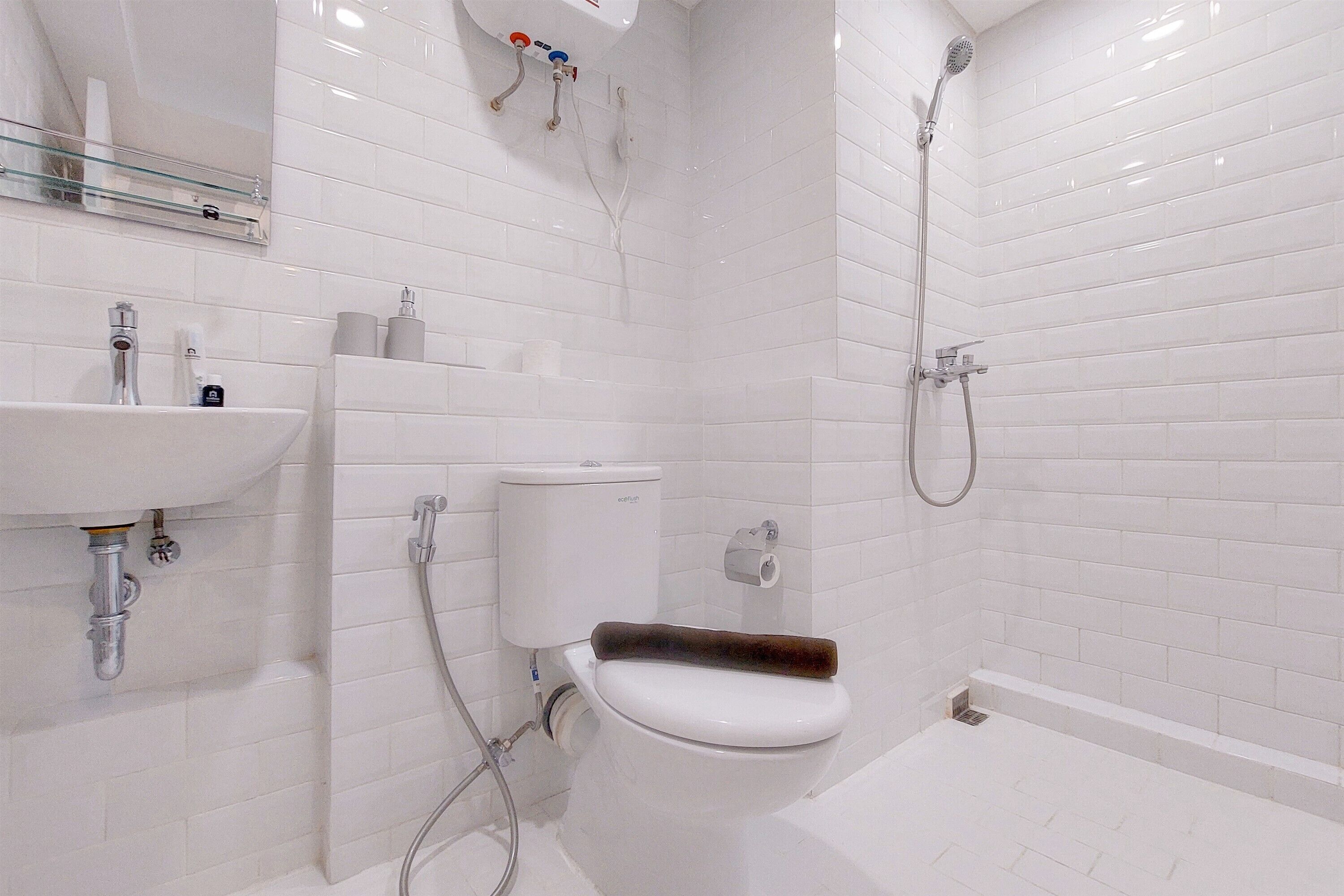 A bathroom with a white tiled wall, a sink, a toilet, and a shower area.