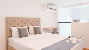 Una cama bien hecha con cabecera capitonada, una mesita de noche con lámpara y una ventana con cortinas.