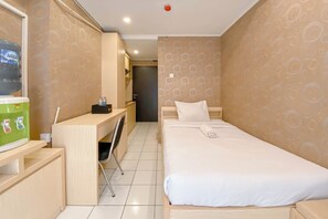 A hotel room with a bed, a desk, a chair, a water dispenser, and a door. - Stylish Studio Apartment At Grand Asia Afrika (Bandung)