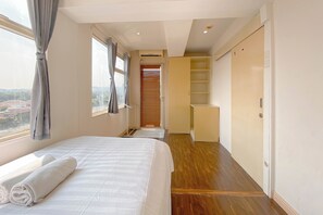 Ein Hotelzimmer mit Bett, Kleiderschrank, einer kleinen Sitzecke und Blick auf die Stadt durch das Fenster.