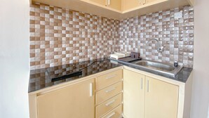 A kitchen with beige cabinets, a black countertop, and a tiled backsplash. - Spacious 1Br At Jarrdin Cihampelas Apartment (Bandung)