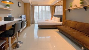 Une chambre d’hôtel moderne, équipée d’un lit, d’un canapé, d’un bureau et de chaises. On y trouve également des étagères avec des plantes et une horloge au mur.
