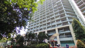 Un hôtel à plusieurs étages, doté d’une façade incurvée, d’une entrée sécurisée par un portail et entouré de verdure.