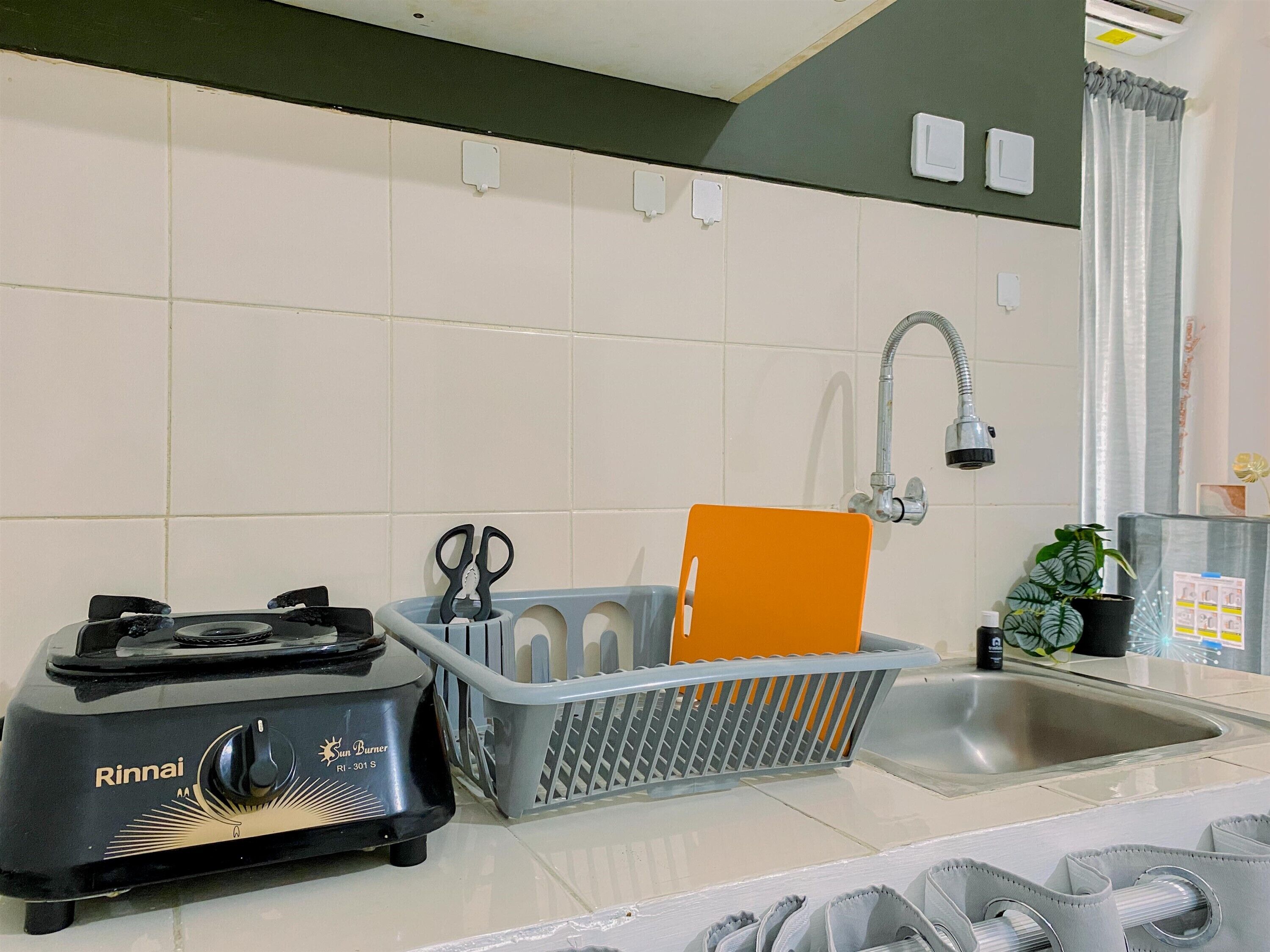Una cocina con una estufa Rinnai Sun Burner, un escurreplatos gris, un lavamanos y un grifo.