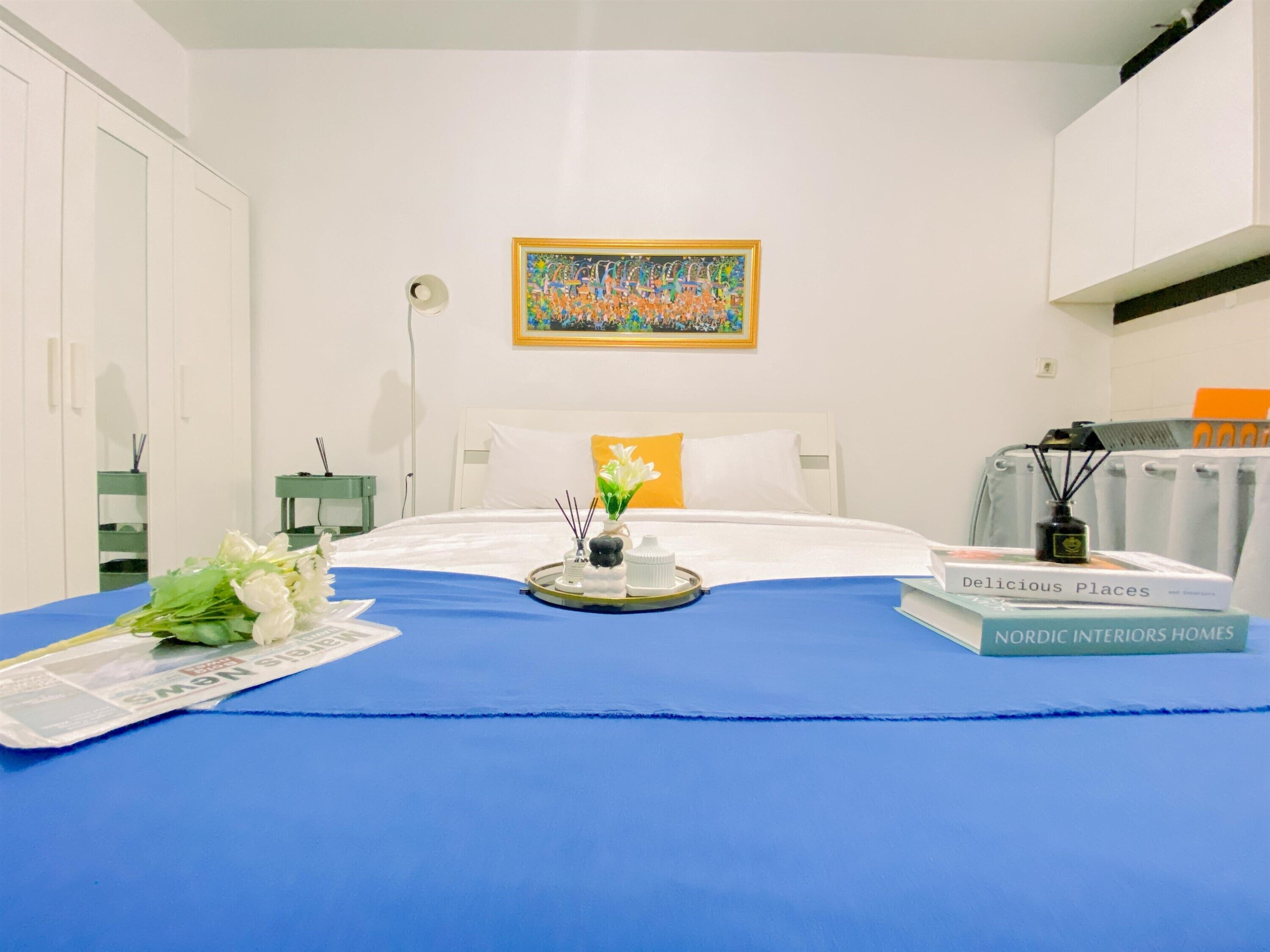 A neatly arranged hotel room with a bed, a bedside table with a lamp, a framed painting on the wall, and a bouquet of flowers on the bed.