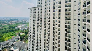A high-rise residential building with multiple balconies, a view of a green landscape, and a distant cityscape.