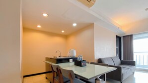 A compact hotel room with a kitchenette, a dining table with chairs, a sofa, and a large window offering a view. - Clean 2Br At Braga City Walk Apartment (Bandung)
