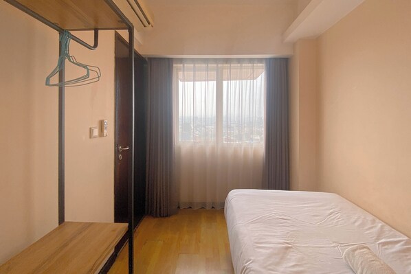 A bedroom with a bed, a wooden bench, a wardrobe, and a view through a window with curtains.