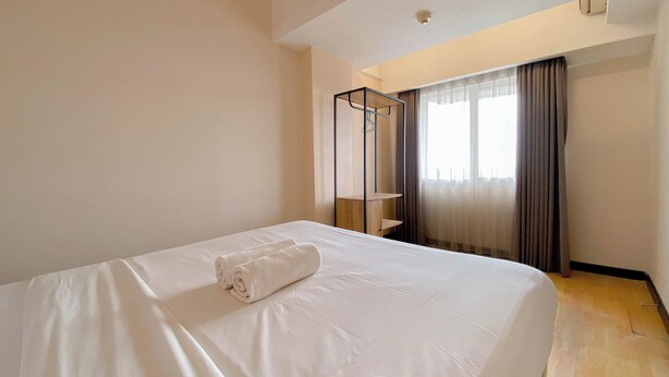 A hotel room with a neatly made bed, a standing mirror, and a window with curtains. - Clean 2Br At Braga City Walk Apartment (Bandung)