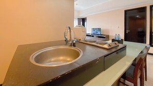 A modern kitchen with a stainless steel sink, a built-in oven, and a flat-screen TV. - Clean 2Br At Braga City Walk Apartment (Bandung)