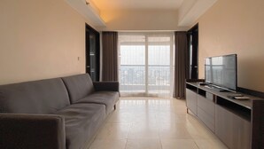 A modern living room with a grey sofa, a flat-screen TV on a wooden stand, and a balcony with a view. - Clean 2Br At Braga City Walk Apartment (Bandung)