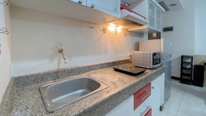 A kitchen with granite countertops, a stainless steel sink, white cabinets, and a microwave. - The Cozy Cranny 2Br At Galeri Ciumbuleuit 1 Apartment (Bandung)