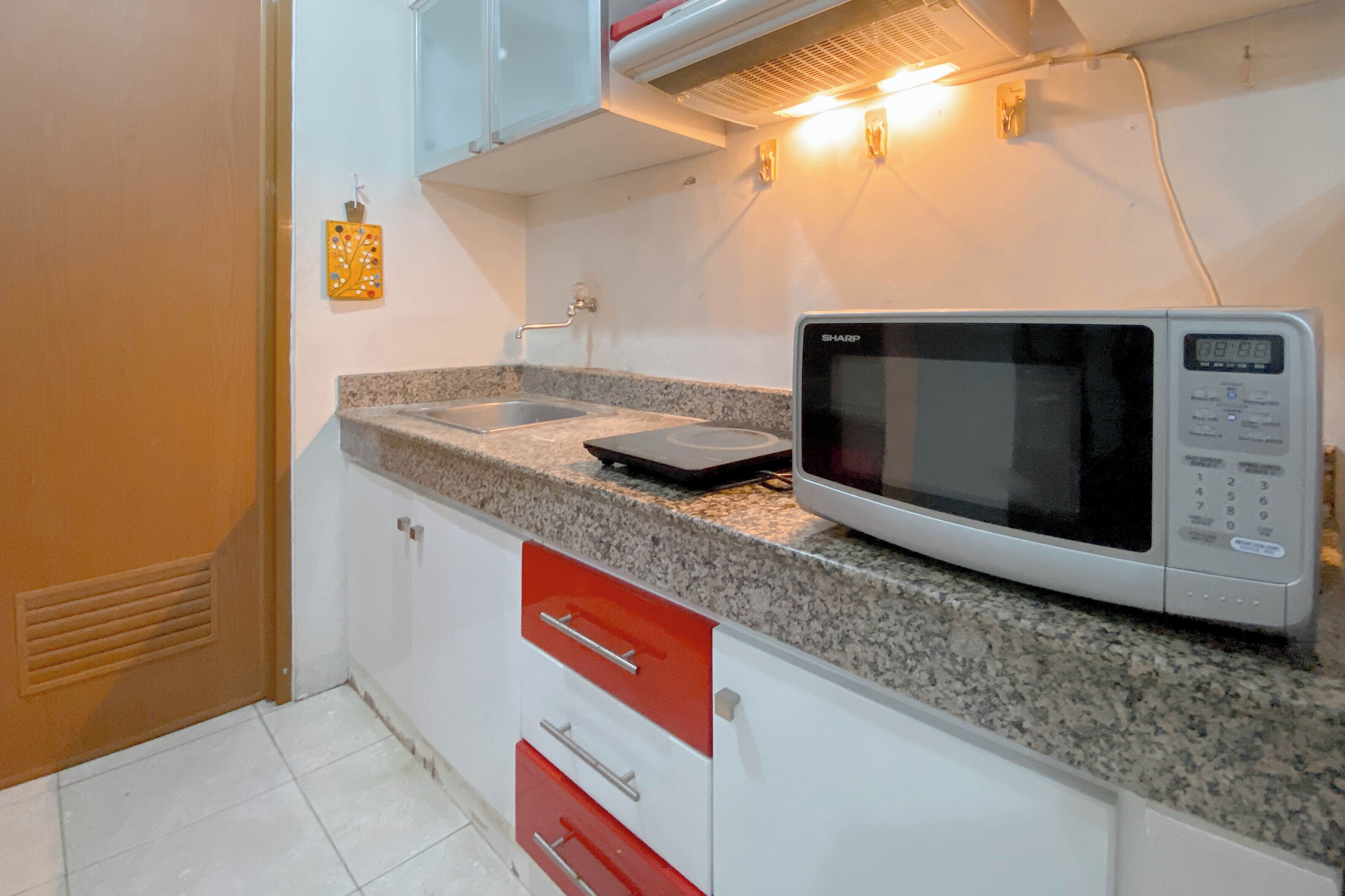 Une cuisine équipée d’un four à micro-ondes, d’un plan de travail en granit, de meubles blancs et d’un tiroir rouge.