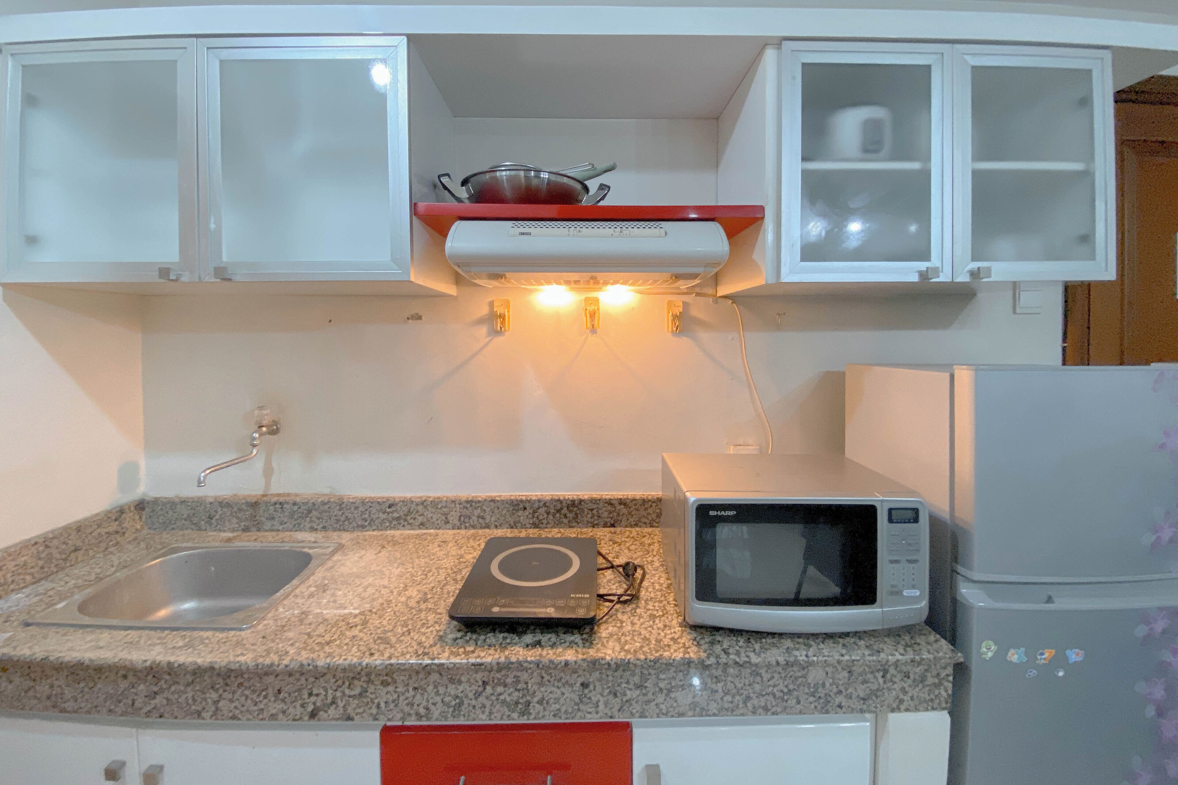 Una cocina con encimera de granito, microondas, refrigerador, pileta y alacenas sobre la encimera.
