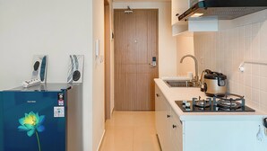 A compact kitchen with a refrigerator, stove, sink, and wooden door. - Minimalist And Cozy Studio Tamansari Iswara Apartment (Bekasi)