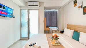 A hotel room with a bed, a TV mounted on the wall, a desk, and a window with curtains. - Minimalist And Cozy Studio Tamansari Iswara Apartment (Bekasi)