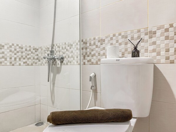 A bathroom with a shower, toilet, and a towel on the floor.