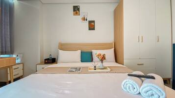 Una cama bien hecha con sábanas blancas, un cojín color turquesa y un florero sobre una mesita de noche.
