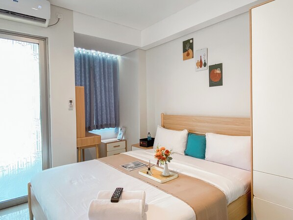 A hotel room with a bed, a bedside table, a desk, a chair, a window with curtains, and wall art.