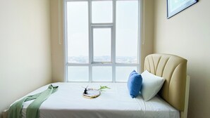 A neatly made bed with a green towel, a blue pillow, and a small plant. - Modern Look 2Br At Lucky Tower Residence Apartment (Jakarta)