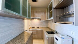 A compact kitchen with wooden cabinets, a stainless steel range hood, a built-in oven, a sink, and a compact dishwasher. - Modern Look 2Br At Lucky Tower Residence Apartment (Jakarta)