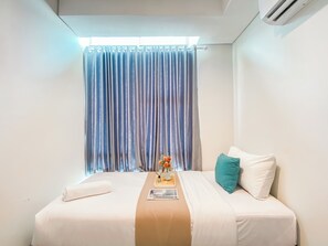 A neatly made bed with white bedding and a beige accent, a teal pillow, and a small vase with flowers on the nightstand. - Spacious And Comfort 2Br Tamansari Iswara Apartment (Bekasi)