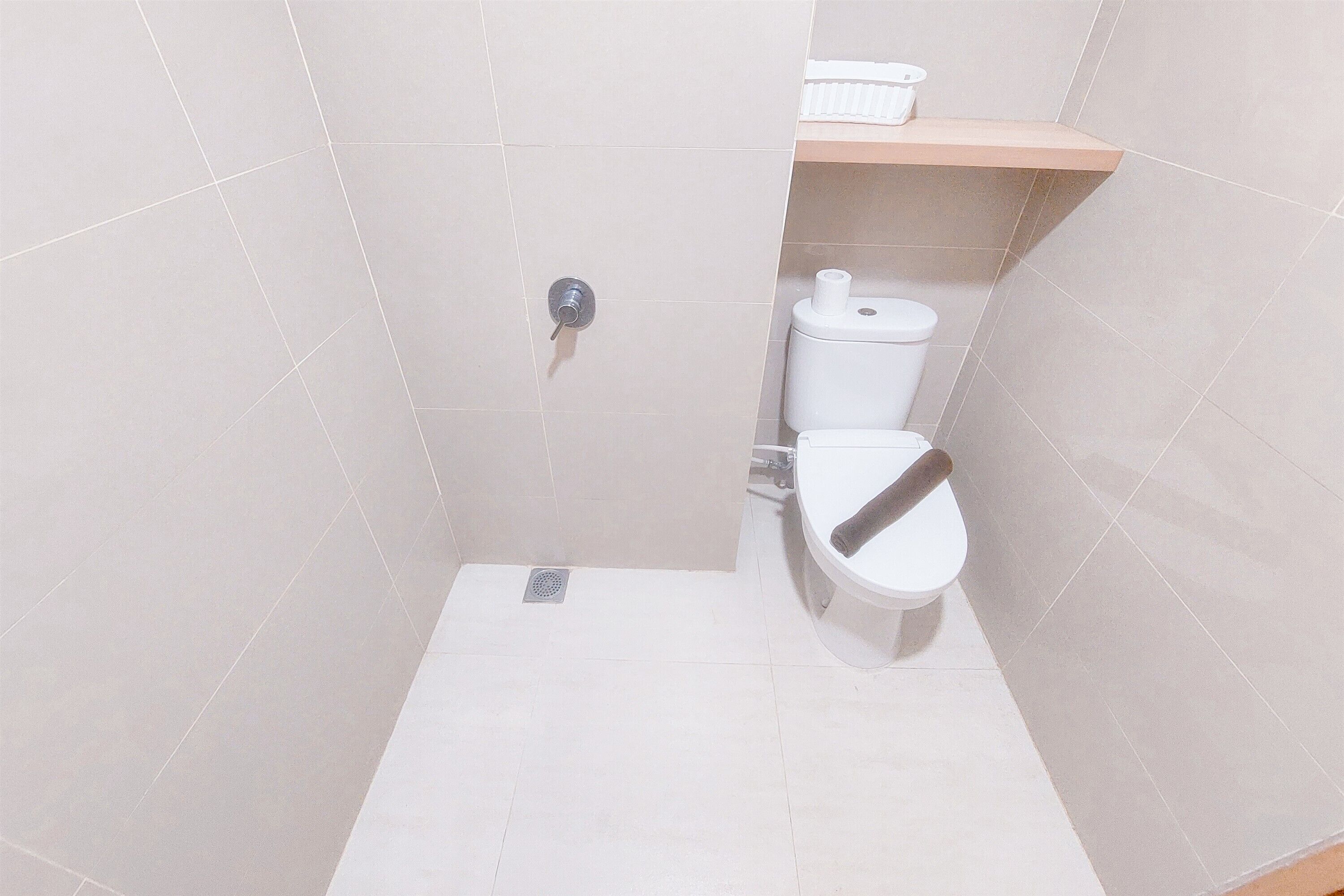 A bathroom with a toilet, a shower, and a shelf with a tissue box.