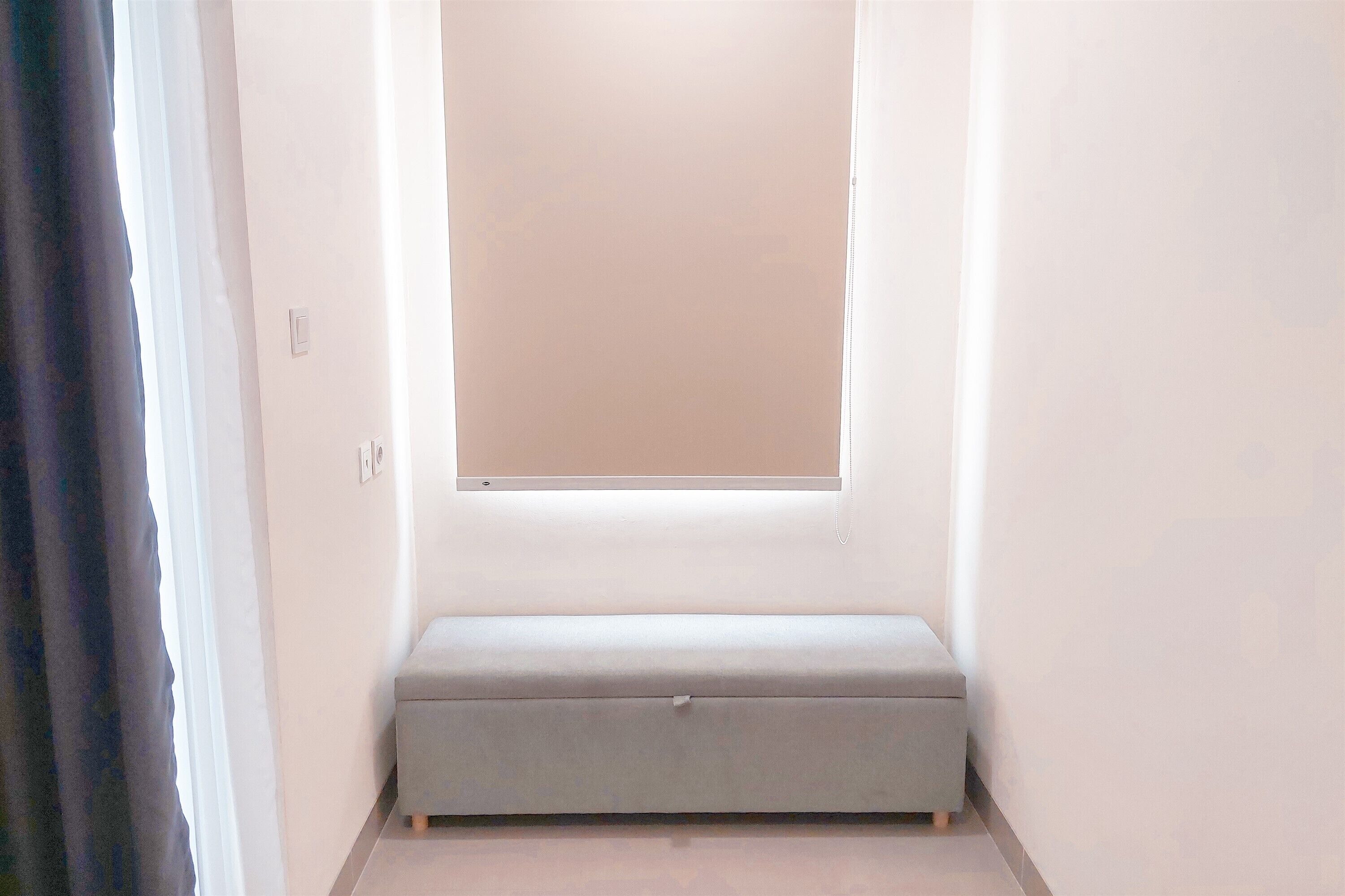 Um espaço pequeno e estreito, com um banco, uma janela e uma porta.