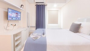 A hotel room with a bed, a desk with a computer, a TV mounted on the wall, and a window with curtains. - Good Place And Relaxing Studio Apartment At B Residence (Pagedangan)