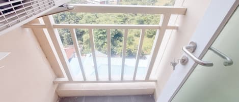 A balcony with a view of a cityscape, a white door with a handle, and an air conditioning unit.