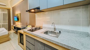Una cucina moderna con piani in granito, lavello in acciaio inossidabile e piano cottura a gas. Si nota un mobiletto in legno sopra il lavello e un piccolo televisore a parete.