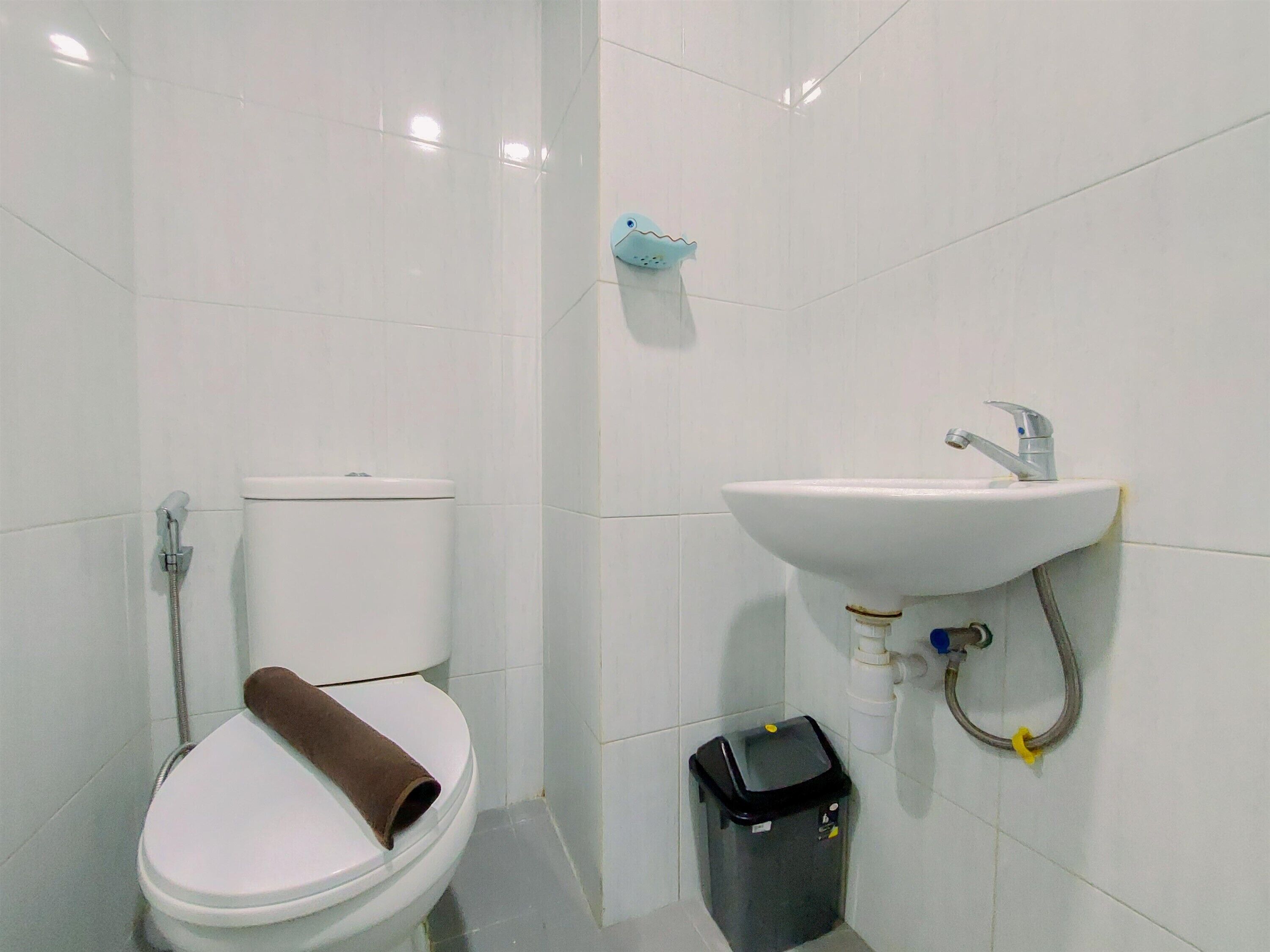 A bathroom with a toilet, a sink, and a trash bin.
