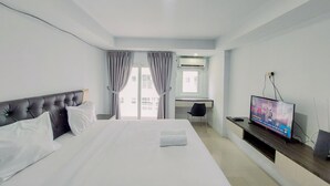 Una habitación de hotel moderna con una cama grande, un escritorio, televisión y ventana con cortinas.