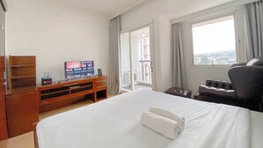 Una habitación de hotel con cama, televisor sobre un soporte de madera, ventana con vistas y puerta al balcón.