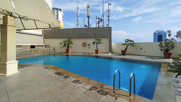 Una piscina en la azotea con plantas en macetas y vistas del horizonte de la ciudad.