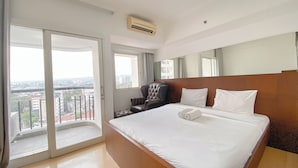 Habitación de hotel con una cama grande, una silla, un escritorio y vista de la ciudad desde un balcón.