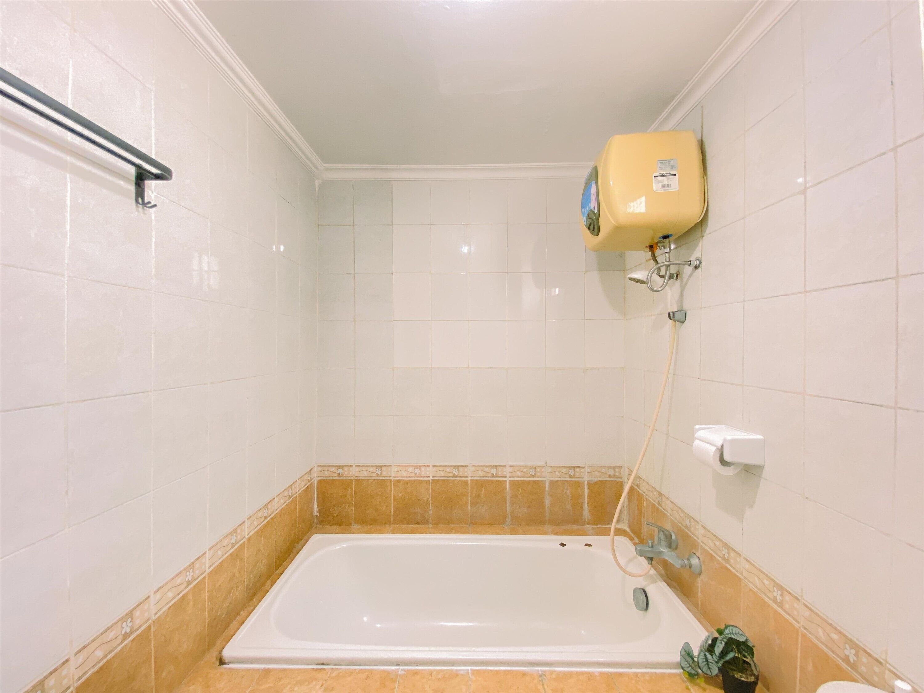 A bathroom with a bathtub, a towel rack, a toilet, and a showerhead.