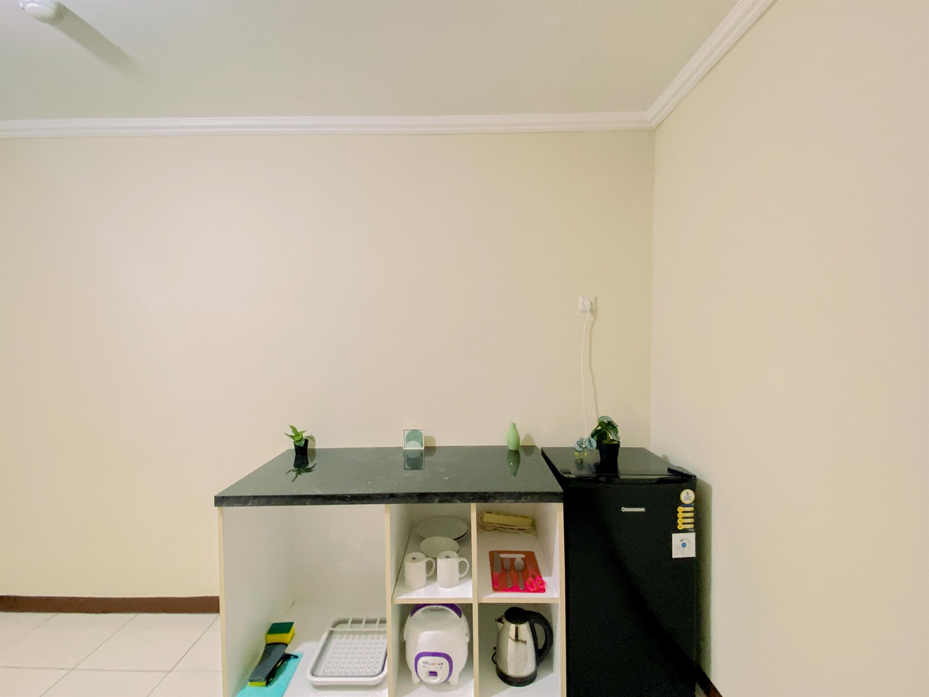 A compact kitchen with a black countertop, a coffee maker, a kettle, and a refrigerator.