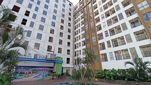 A multi-story residential building with balconies, a swimming pool, and a mural advertising a nearby attraction. - Good Deal And Restful 1Br Apartment Tamansari Skylounge Makassar (Makassar)