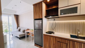 A modern kitchen with wooden cabinets, a built-in oven, and a microwave. There is a dining area with a table and chairs, and a balcony with a view. - Good Deal And Restful 1Br Apartment Tamansari Skylounge Makassar (Makassar)