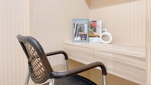 A wicker chair with a metal frame, a white wall with a subtle pattern, and a shelf with books and a vase.
