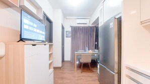 A narrow hallway with a flat-screen TV on a shelf, a dining table with chairs, and a refrigerator. - Good And Modern 2Br At Citra Living Apartment (Jakarta)