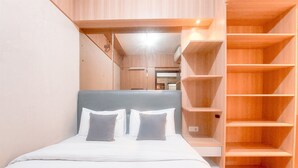 A bedroom with a bed, two pillows, a headboard, and built-in wooden shelving. - Good And Modern 2Br At Citra Living Apartment (Jakarta)