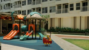 A playground with slides and a play structure, surrounded by a building with balconies. - Good And Modern 2Br At Citra Living Apartment (Jakarta)