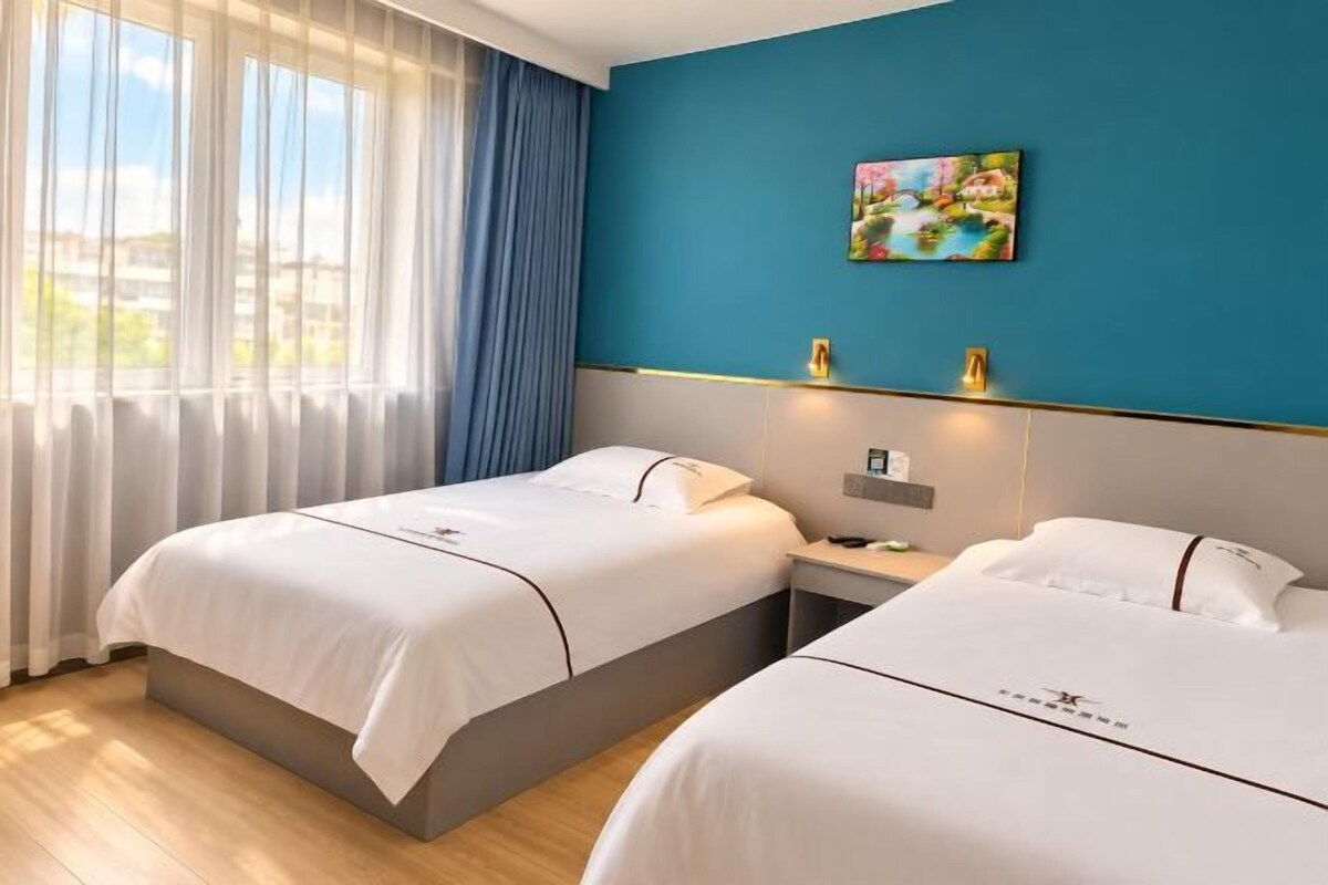 Ein Hotelzimmer mit zwei Betten, einem Nachttisch, einem Gemälde an der Wand und einem Fenster mit Vorhängen.